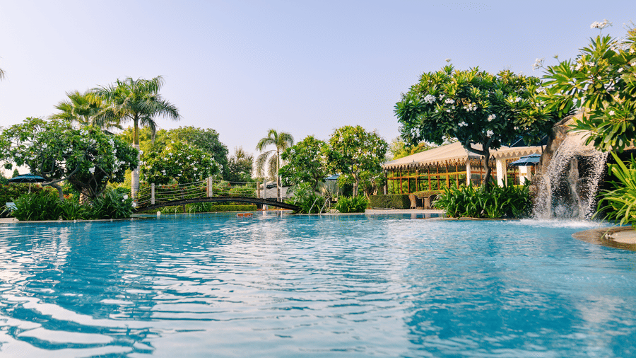 Swimming pool with a small waterfall on the side and a bridge in the centre